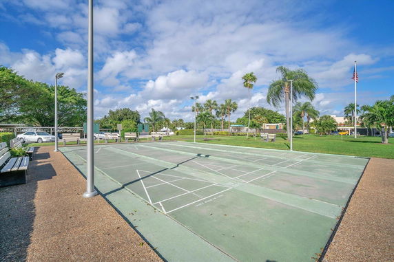 Outdoor view of shuffleboard courts with benches and surrounding palm trees.
