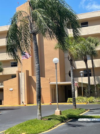 Front view of a multi-story building with palm trees and a parking area.