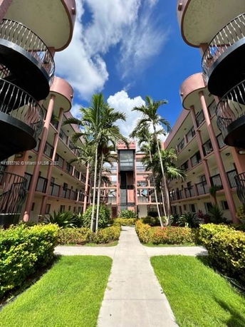 View of a multi-story building with balconies and palm trees in the courtyard.