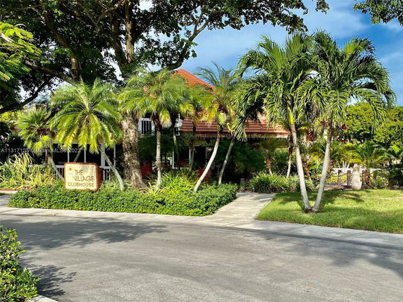Front view of a clubhouse surrounded by palm trees and greenery.