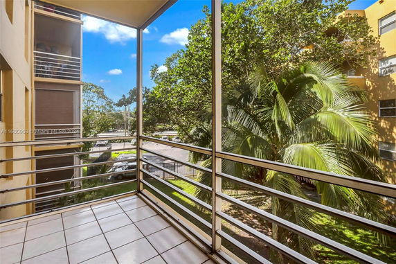 Balcony with railing overlooking trees and a parking area.
