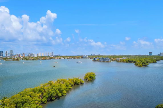 Wide-angle view of a waterfront area with lush greenery and several buildings in the distance.