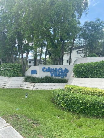 Front view of a residential complex with a sign reading 'Calusa Club Village', surrounded by greenery.