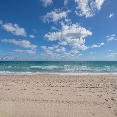 Beach view with ocean waves and cloudy sky.