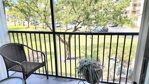View from a balcony showing trees, grass, and parked cars in a residential area.