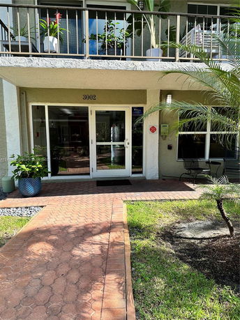 Front view of a building entrance with balcony and potted plants.