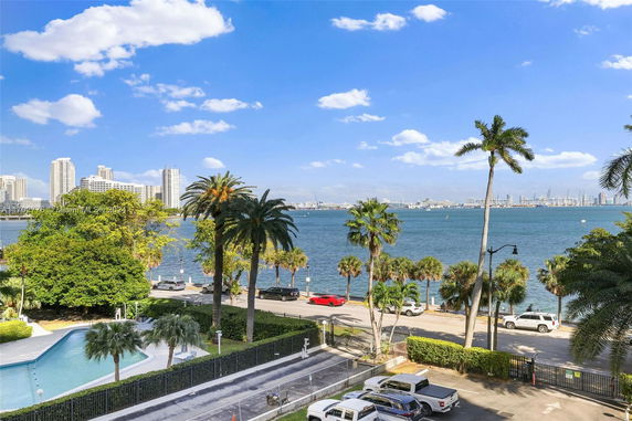 Wide angle view of a waterfront cityscape with high-rise buildings and palm trees lining the shoreline.
