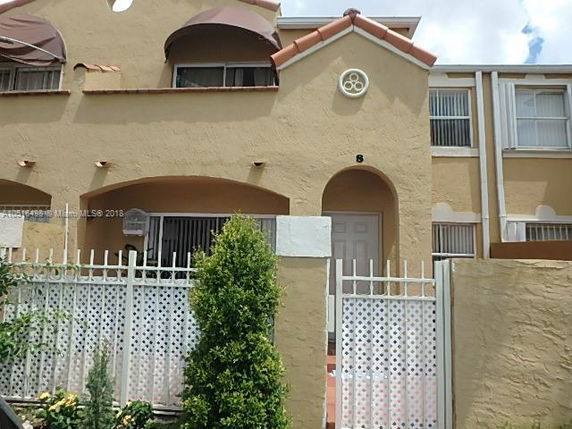 Front view of a two-story house with arched entryway and wrought iron gate.