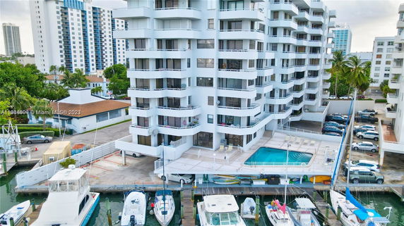 View of a multi-story residential building with balconies, located near a waterfront with docked boats and a swimming pool area.