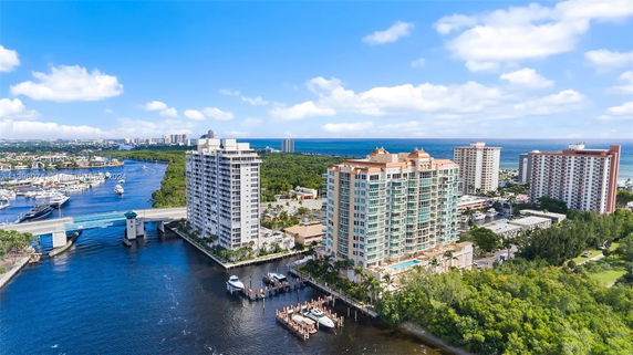 Aerial view of high-rise buildings near a river and marina, with ocean in the background.
