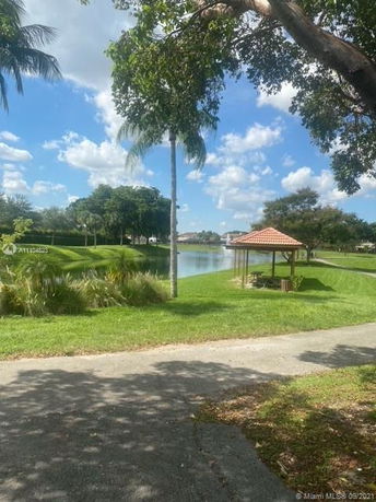 View of a park area with a lake and gazebo surrounded by trees and grassy landscape.