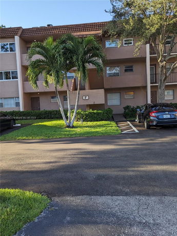 Front view of a multi-story residential building with balconies and parking area in front.