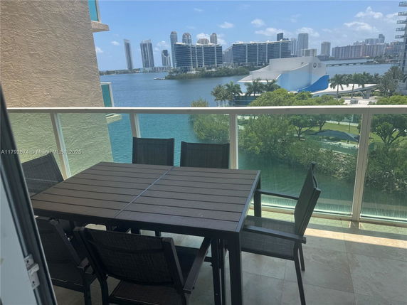 Balcony area with a dining table set overlooking a body of water and cityscape.