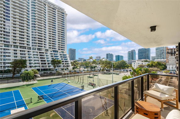 Panoramic view from a balcony overlooking a tennis court and multiple high-rise buildings.
