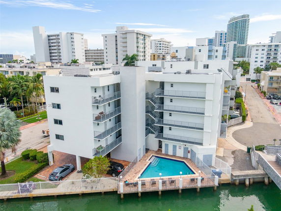 Front view of a multi-story apartment building with balconies and a small pool area.