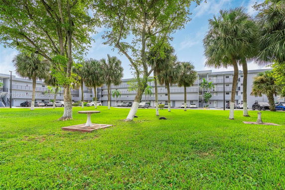 View of a multi-story residential building with a grassy area and trees in the foreground.