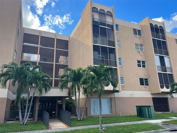 Front view of a multi-story residential building with balconies and palm trees.