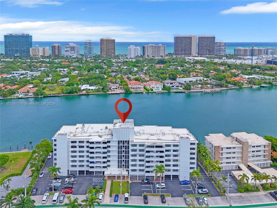 Aerial view of a multi-story residential building near a waterfront with a cityscape in the background.