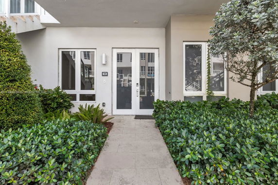 Front entrance of a building with glass doors and windows, surrounded by greenery.