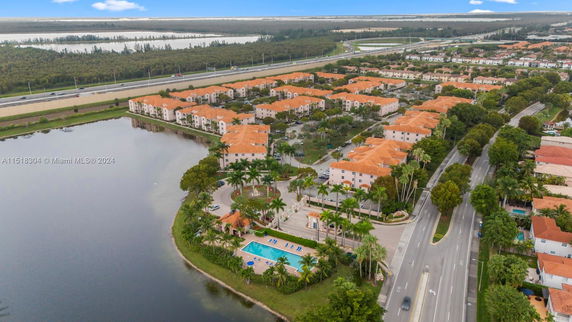 Aerial view of a residential complex with orange-roofed buildings surrounding a swimming pool next to a large water body.