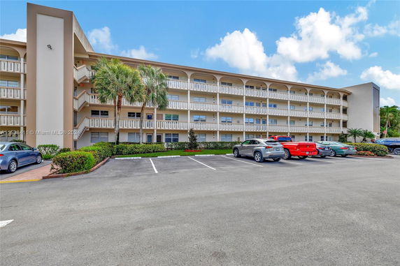 Front view of a multi-story apartment building with balconies and parking area.