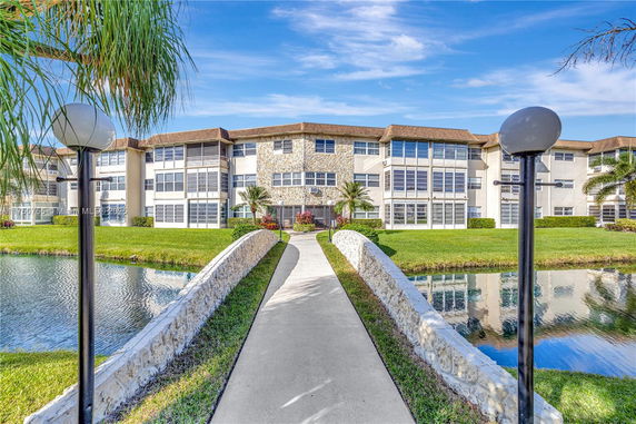 Front view of a multi-story residential building with a walkway and small bridge over water.