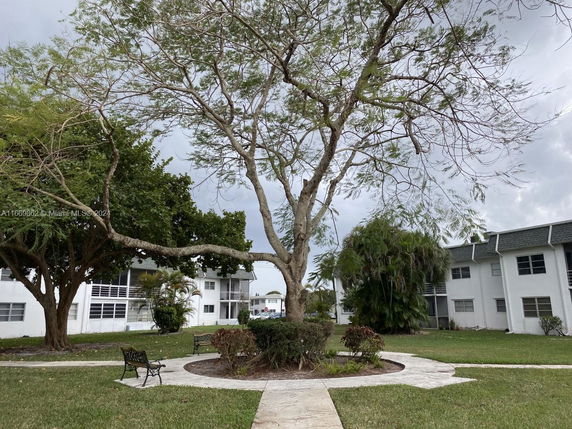 View of residential buildings with a central courtyard featuring a large tree and benches.