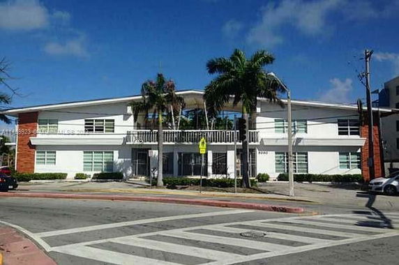 Front view of a two-story building with palm trees and a balcony.