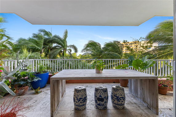 View from a balcony with a wooden table and decorative stools, overlooking palm trees and surrounding buildings.