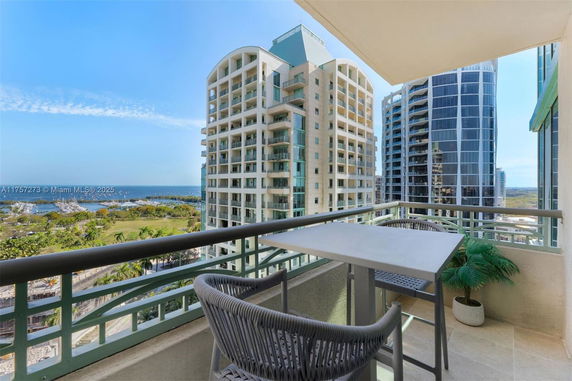 Panoramic view from a balcony, showing nearby high-rise buildings and ocean in the distance.