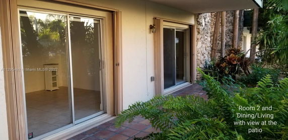 Exterior view showing sliding glass doors and a stone wall with surrounding greenery.