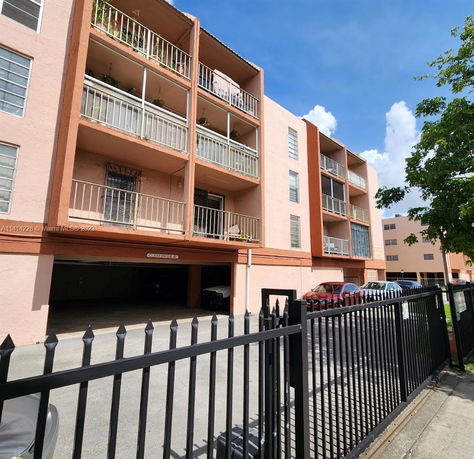 Front view of a multi-story apartment building with balconies and a gated entrance.