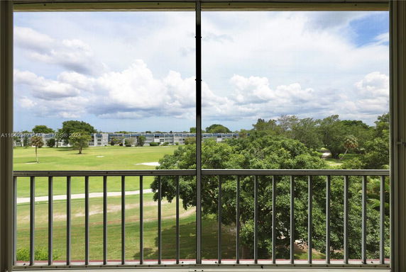 View through a window showing a green landscape and distant buildings.