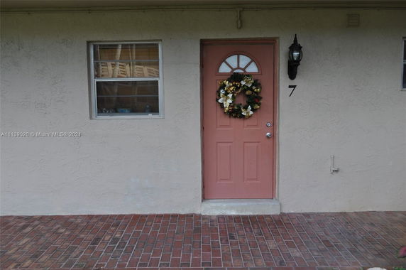 Front view of a house entrance with a wreath on the door and a wall-mounted lamp.