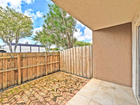 Outdoor area with a brick-patterned ground and wooden fence, adjacent to a building wall.
