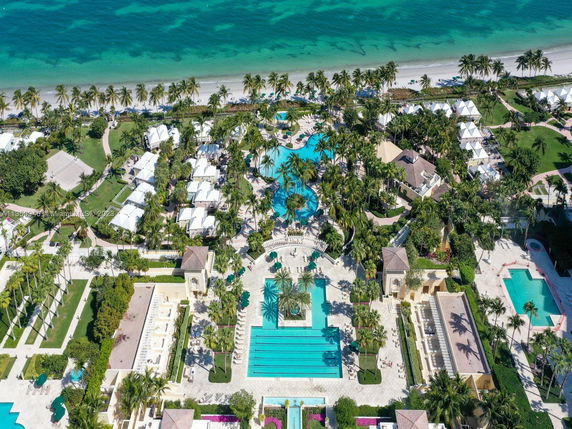 Aerial view of coastal resort area with swimming pools and palm trees near the ocean.