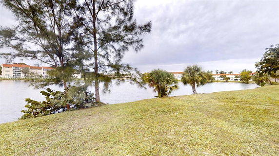 View of buildings across a water body with trees and grass in the foreground.