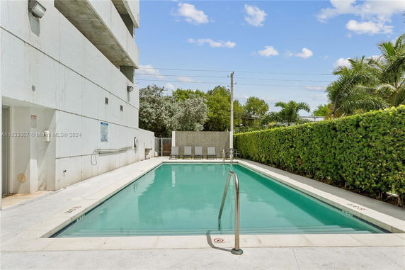 View of a building with a swimming pool, surrounded by hedges and trees.