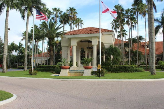 Front view of a large building with a red-tiled roof and columns, surrounded by palm trees.