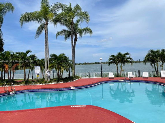 Outdoor swimming pool with palm trees and a view of a lake.