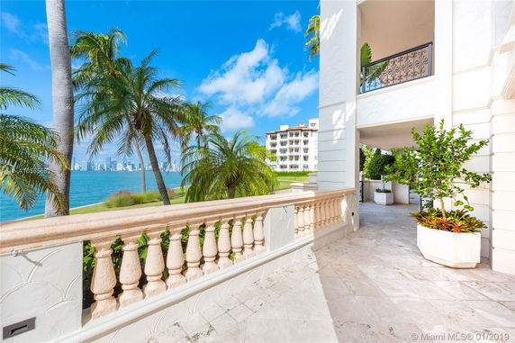 Exterior view of a waterfront residential building with a balcony, overlooking a body of water and cityscape in the distance.