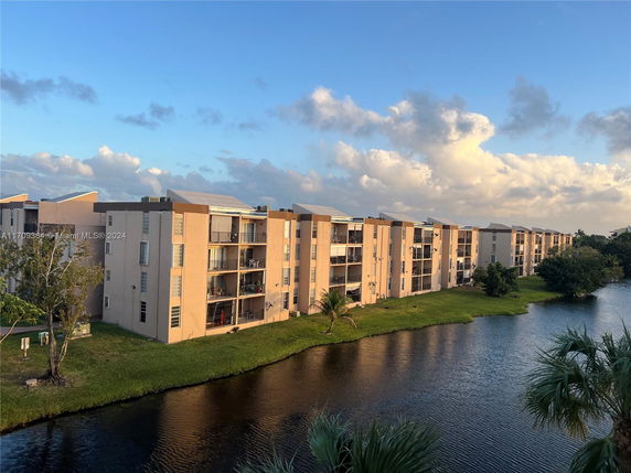 Apartment buildings alongside a water body with trees and green grass.
