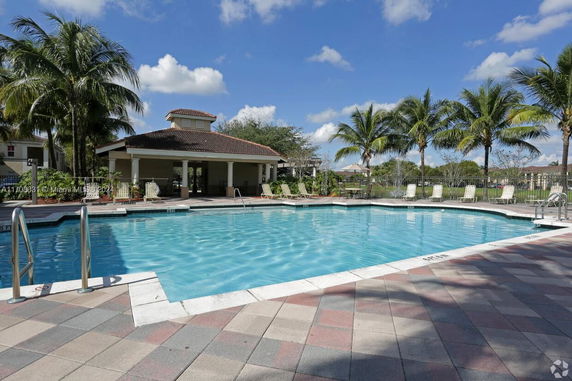 Outdoor swimming pool area with lounge chairs and a small building.