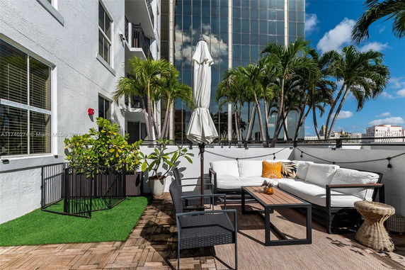 Rooftop patio with outdoor seating and decorative plants, surrounded by urban buildings.