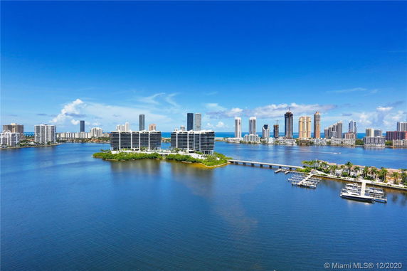 Panoramic view of waterfront cityscape with modern buildings and a bridge over the water.