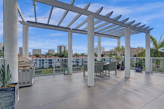 Rooftop patio with pergola, outdoor seating, and a grill, offering views of surrounding buildings.