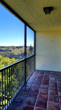 Balcony with a tiled floor and metal railing, overlooking a view of treetops and distant buildings.
