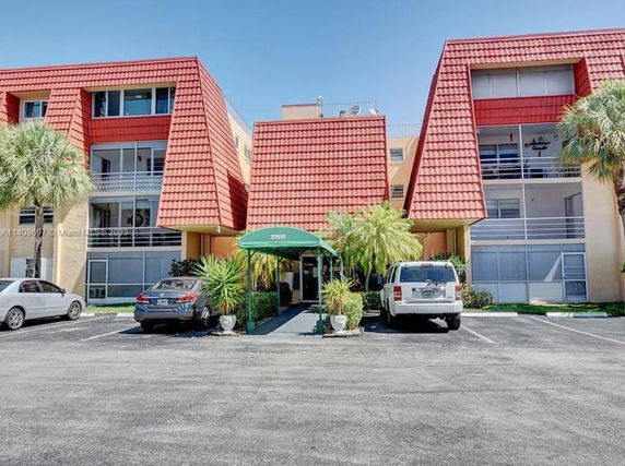Front view of a multi-story residential building with red roofs and parking area in front.