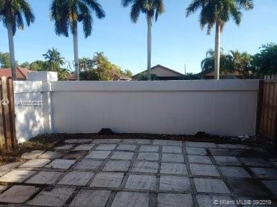 Outdoor paved area in a residential backyard with palm trees in the background.