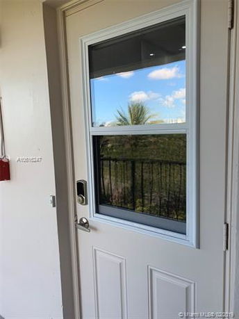 A door with a window showing foliage and some sky in the reflection, indicating a view from or towards a building's surrounding area.